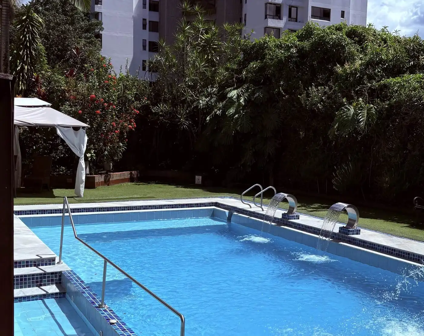 Piscina exterior de Akzara, jardín y edificio de fondo